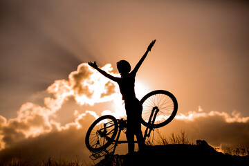 Happy cyclist woman silhouette over dramatic cloudy sky