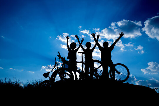 Happy family with bike and hands up over sunset dramatic clody sky 