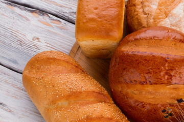 Fresh bakery products background. Traditional bread, baguettes and buns on wooden background close up.