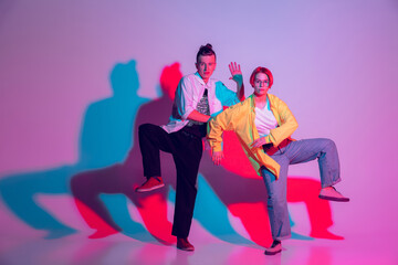 Obraz premium Young man and woman, couple dancing hip-hop, street style isolated on studio background in colorful neon light. Fashion and motion, youth, music, action concept. Trendy clothes. Copyspace for ad.