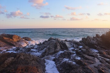 Sea water flowing down rocks with ocean and sunset in the background