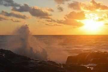 Giant splash from wave crashing against rocks at sunset