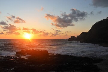 Fototapeta na wymiar orange sun touching the sea surface at sunset at beautiful rocky coast