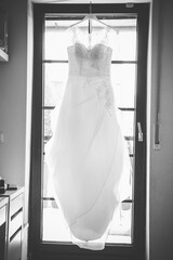 Wedding dress is hanging from the ceiling on front of a bed