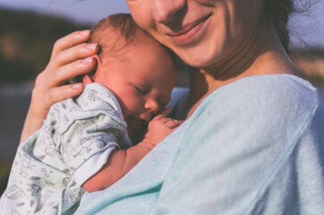 Portrait of a young mother with a baby in her arms outdoors in summer