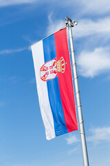 Flag of Serbia waving in the wind against white cloudy blue sky