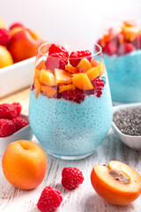 Layered superfoods pudding with apricot, raspberry, chia in glasses on white wooden background. Mousse with chia seeds, berries and fruits for healthy breakfast, top view