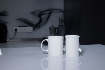 two white cups with tea and sticking out tea bags on a white table in a gray kitchen. High quality photo