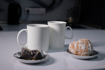 two white cups of tea next to used tea bags next to gingerbread cookies on a white table in a gray kitchen. High quality photo