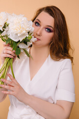 Girl model in a white dress with curls holding peonies in her hands