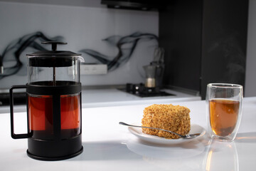  cup of tea in a double-botoom glass, french-press teapot and piece of cake on white table in gray kitchen. High quality photo