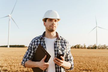 Fototapeta premium An electrical engineer standing on a field with windmills
