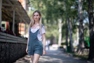 girl in overalls walks in the summer on the street