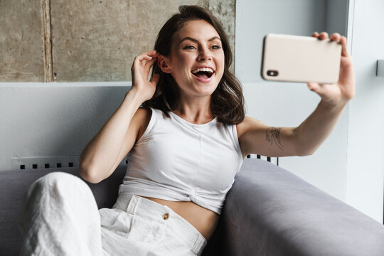 Image of woman taking selfie on smartphone while resting on couch