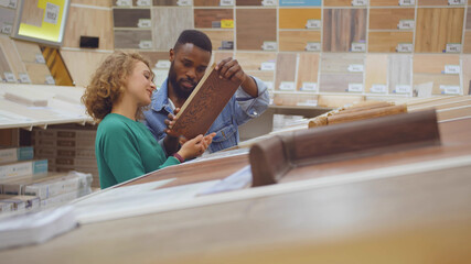 Diverse couple looking at parquet board for home flooring in store