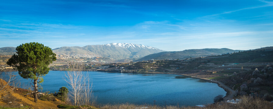 Beautiful panoramic view of Lake Ram (Birkat Ram) - a crater lake (maar) in the northeastern Golan Heights, with a Druze town of Majdal Shams and a snow-capped Mount Hermon in the background