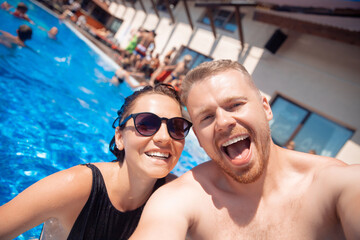 Cheerful happy couple guy and woman make selfie photo in hotel pool, summer vacation travel