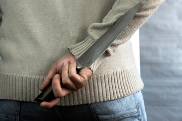 An evil man holds a knife behind his back, waiting for the victim. A maniac and a rapist with a gun.