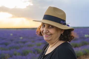 Woman smiling wearing a hat with short curly hair at a lavender field with beautiful sunset