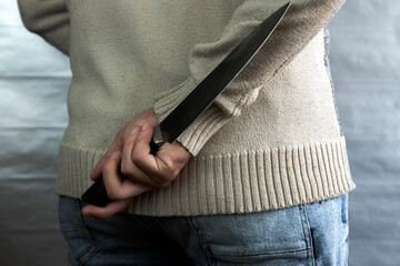 An evil man holds a knife behind his back, waiting for the victim. A maniac and a rapist with a gun.