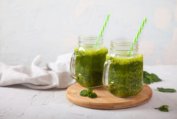 Two jars with green smoothies on a wooden stand on a concrete gray background. Healthy eating. Detox. Copy spaes