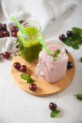 Green and sweet cherry smoothies on a wooden stand, scattered cherries and a linen napkin on a concrete background. Flat lay.