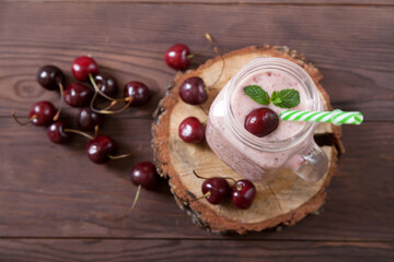 Obraz na płótnie Canvas Sweet cherry smoothies in a jar with a straw, scattered berries on a wooden background. Vegetarian food. Healthy eating.