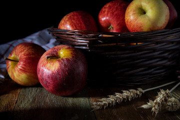 
Red apples in a wicker basket and on a wooden table in rustic style