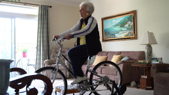 Elderly woman doing workout on exercise bicycle in front of television.