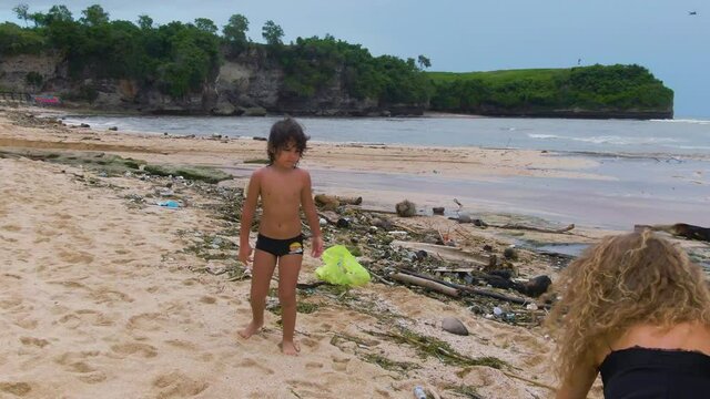 Environment Problem. Cleaning Up Beach From Plastic Pollution. Mother And Child Picking Up Garbage And Solid Waste For Recycling. Side View Of Young Woman And Boy Cleaning Up Ocean Coast.