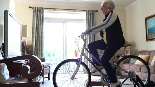 Low angle view of senior elderly woman on exercise bicycle in front of television.
