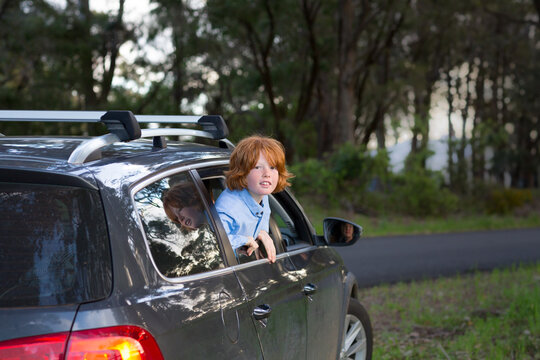 Child leaning out of car window on the side of the road
