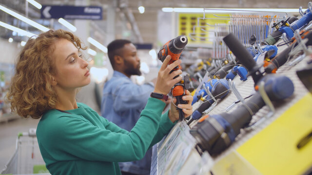 Young woman choosing electric screwdriver in hardware store