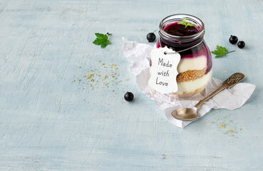 Layered curd dessert jar. Cottage cheese mousse with berry sauce in a glass jar with a spoon and black currant berries on a light blue background with space for text. Top view