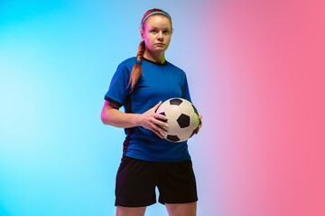 Confident posing. Female soccer, football player training in action isolated on gradient studio background in neon light. Concept of motion, action, ahievements, healthy lifestyle. Youth culture.