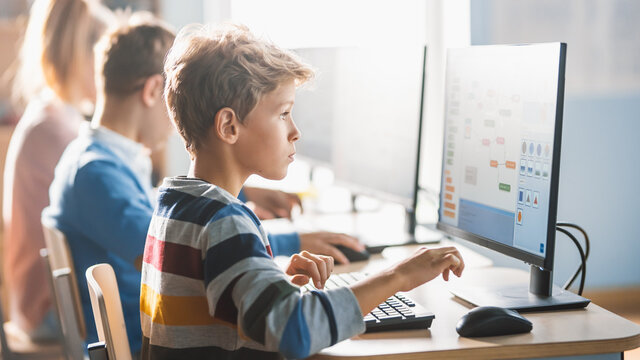 Elementary School Science Classroom: Smart Little Schoolchildren Sitting in Row and Work on Personal Computers, Learn Programming Language for Software Coding. Schoolchildren Getting Modern Education