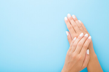 Young woman hands with white nails on light blue table background. Pastel color. Point of view shot. Closeup. Soft touch. Empty place for text. Top down view.