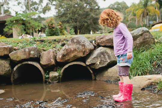 Girl in gumboots playing in a drain
