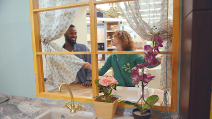 View through window of young diverse couple choosing kitchen sink in furniture store