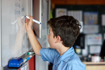 Primary school student in classroom writing on whiteboard