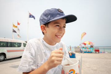 Young boy laughing whilst eating snow cone at beach