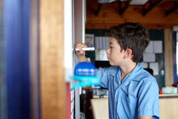 Young school boy writing on a white board in classroom