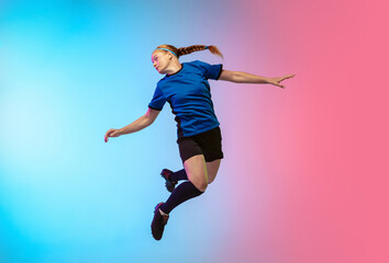 Fototapeta na wymiar High jumping. Female soccer, football player training in action isolated on gradient studio background in neon light. Concept of motion, action, ahievements, healthy lifestyle. Youth culture.