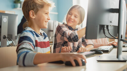 Elementary School Computer Science Classroom: Portrait of Smart Girl and Boy Talking while using Personal Computer, Learning Informatics, Internet Safety, Programming Language for Software Coding