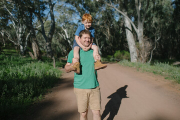A young boy sitting on his fathers shoulders in the bush