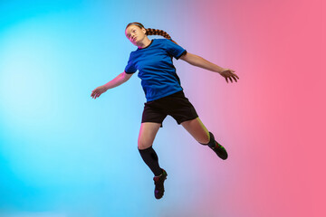 High jumping. Female soccer, football player training in action isolated on gradient studio background in neon light. Concept of motion, action, ahievements, healthy lifestyle. Youth culture.