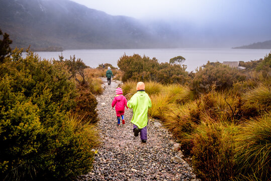 Children in bright rain jackets running down path on overcast day