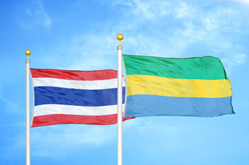 Thailand and Gabon two flags on flagpoles and blue sky