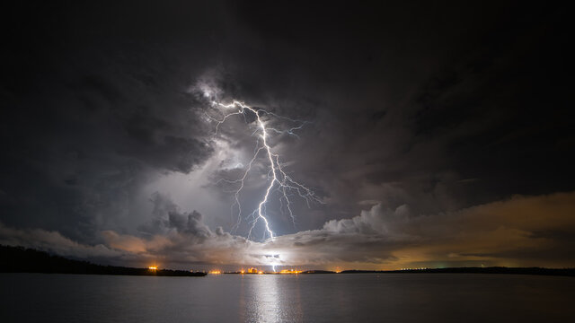 View of lightning over factory with ocean in foreground at night