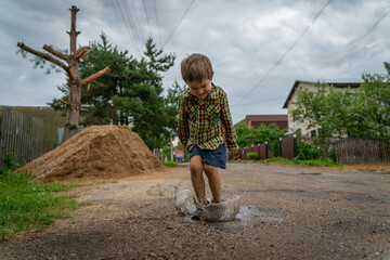 A boy in a shirt and shorts jumps into a puddle